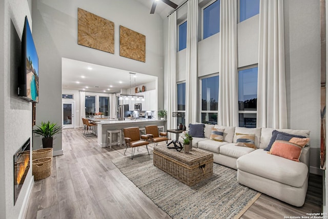 living room featuring a towering ceiling, light wood-style floors, and recessed lighting