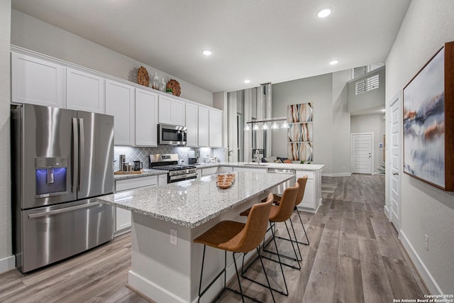 kitchen featuring stainless steel appliances, a peninsula, white cabinets, a center island, and a sink