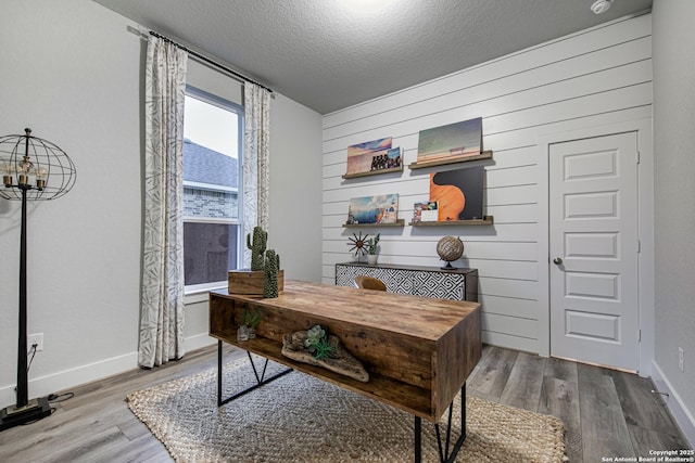office area with wood finished floors, a textured ceiling, baseboards, and wooden walls