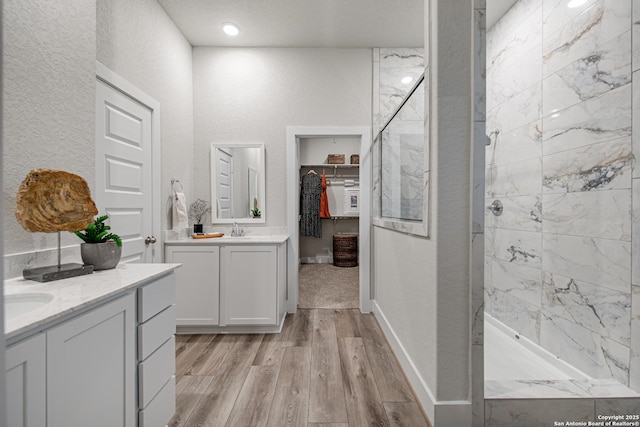 full bathroom with a tile shower, wood finished floors, a textured wall, and two vanities
