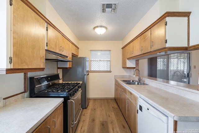 kitchen featuring stainless steel appliances, under cabinet range hood, a sink, light wood-style flooring, and light countertops