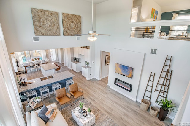 178 Jax Loop, San Antonio, TX 78253 - living room featuring a glass covered fireplace, a towering ceiling, light wood-style flooring, a ceiling fan, and baseboards