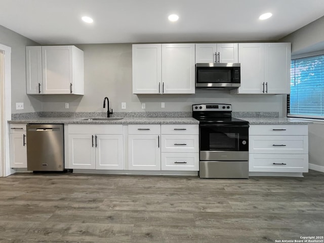 kitchen with stainless steel appliances, a sink, white cabinets, recessed lighting, and light wood-style floors