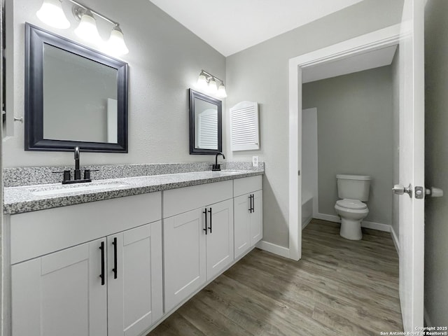 bathroom featuring wood finished floors, baseboards, toilet, and double vanity