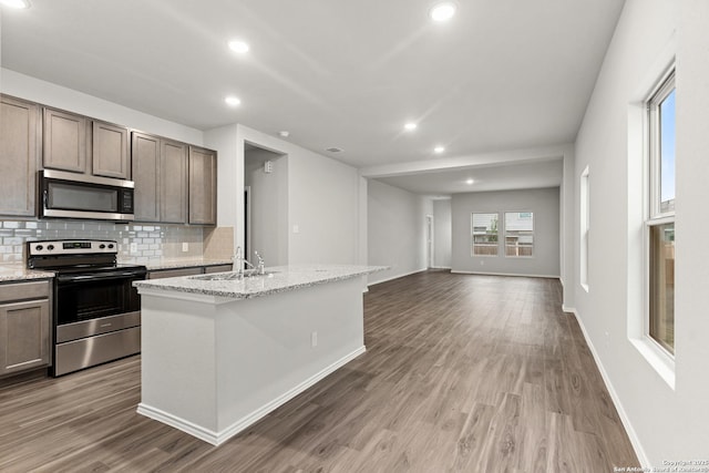 9318 Graze Br, San Antonio, TX 78211 - kitchen featuring stainless steel appliances, a sink, backsplash, wood finished floors, and a center island with sink