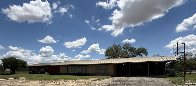 view of front of house with asphalt driveway, an attached carport, a front lawn, metal roof, and brick siding