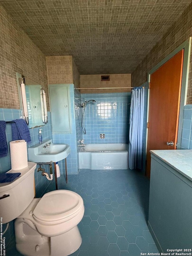 bathroom with shower / tub combo with curtain, toilet, tile patterned flooring, tile walls, and a sink