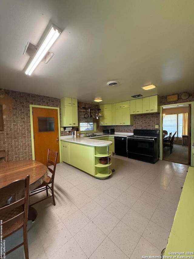 kitchen with green cabinets, black appliances, open shelves, brick wall, and light floors