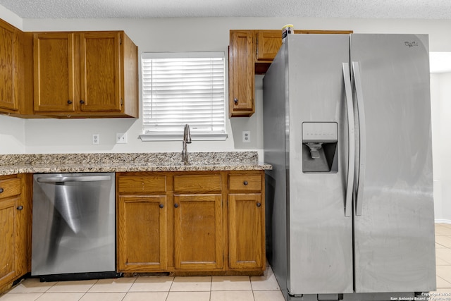 11819 Rousseau, San Antonio, TX 78251 - kitchen featuring appliances with stainless steel finishes, brown cabinetry, light tile patterned flooring, light stone countertops, and a sink