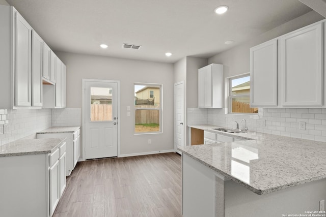 9410 Graze Land, San Antonio, TX 78211 - kitchen with light stone counters, a peninsula, light wood-style flooring, a sink, and white cabinets