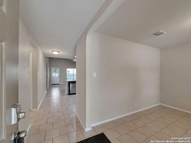 hallway with light tile patterned flooring, baseboards, and arched walkways