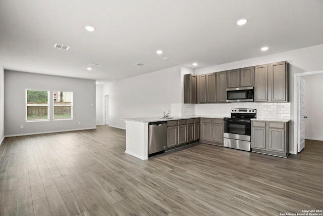 kitchen with stainless steel appliances, open floor plan, a peninsula, tasteful backsplash, and dark wood-style floors