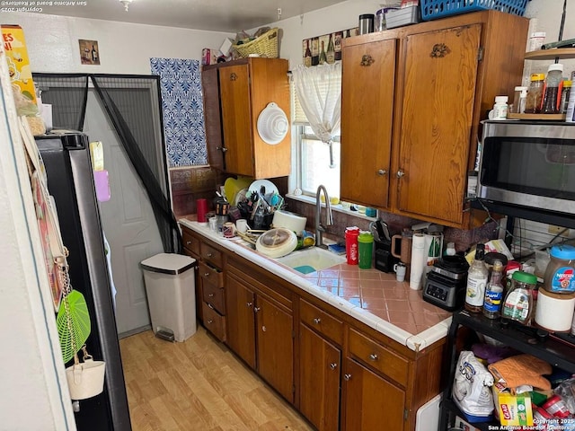 227 E Villaret Blvd, San Antonio, TX 78221 - kitchen featuring appliances with stainless steel finishes, tile counters, light wood finished floors, and brown cabinets