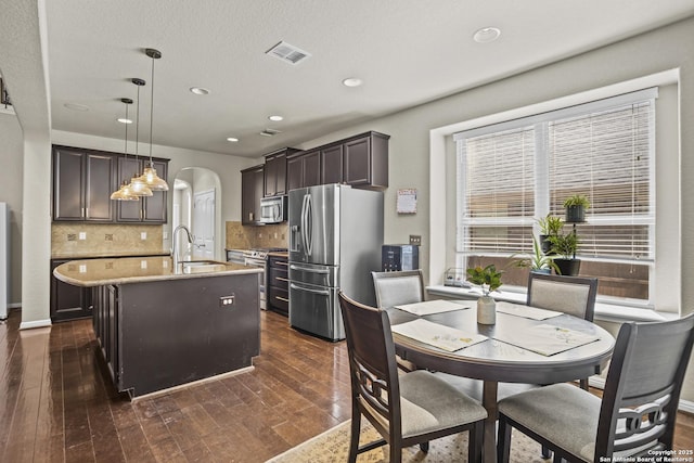 11734 Violet Cv, San Antonio, TX 78253 - kitchen with stainless steel appliances, a sink, an island with sink, arched walkways, and dark brown cabinets