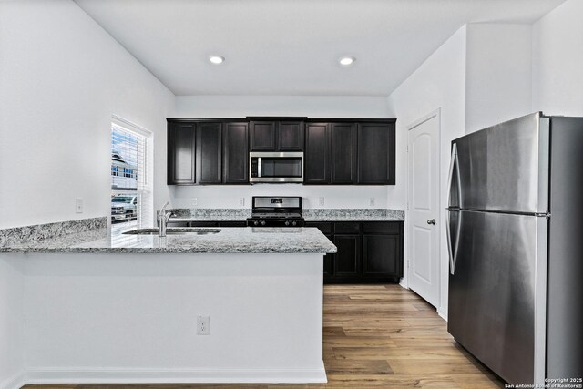 10809 Quinn Ct, San Antonio, TX 78252 - kitchen with appliances with stainless steel finishes, a sink, light wood finished floors, light stone counters, and a peninsula