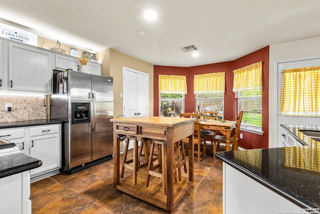 kitchen with stainless steel fridge with ice dispenser, backsplash, dark stone countertops, recessed lighting, and white cabinets