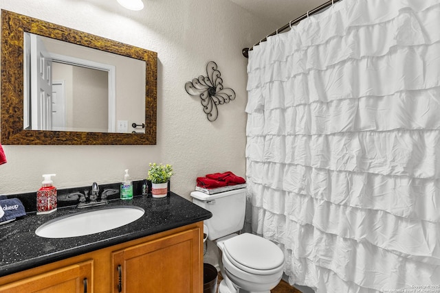 bathroom with vanity, toilet, a textured wall, and curtained shower