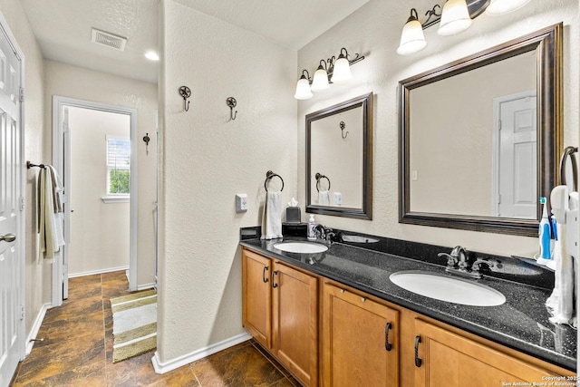 bathroom featuring a textured wall, double vanity, and baseboards