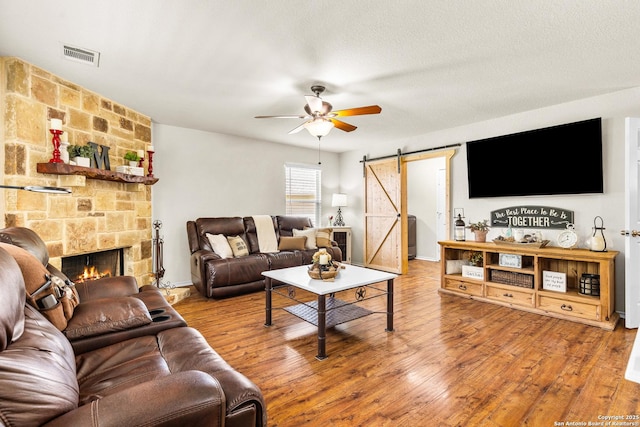 living room with a barn door, a ceiling fan, wood finished floors, and a stone fireplace