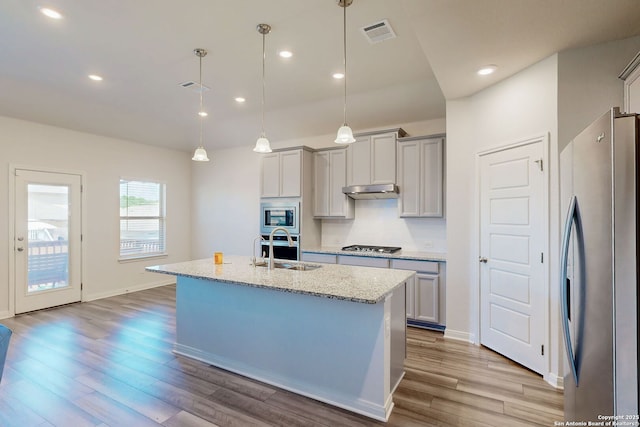 10259 Juniper Oaks, Boerne, TX 78006 - kitchen featuring appliances with stainless steel finishes, a sink, wood finished floors, light stone countertops, and a kitchen island with sink