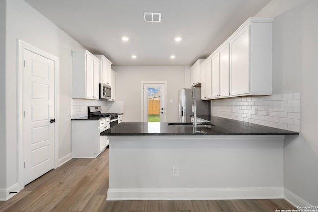 kitchen featuring stainless steel appliances, a peninsula, white cabinetry, decorative backsplash, and recessed lighting