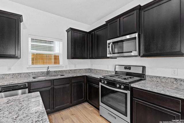 10819 Quinn Ct, San Antonio, TX 78252 - kitchen featuring appliances with stainless steel finishes, a sink, light wood-style floors, light stone countertops, and dark cabinets