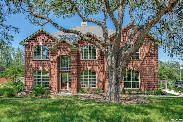 traditional-style home featuring brick siding, a front yard, a chimney, and a shingled roof