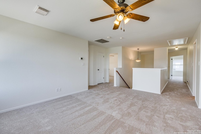 spare room featuring attic access, light colored carpet, baseboards, and ceiling fan