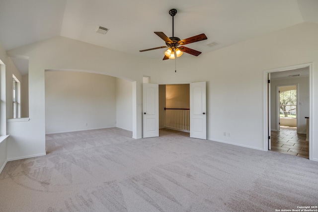 unfurnished bedroom featuring vaulted ceiling, light colored carpet, baseboards, arched walkways, and a ceiling fan