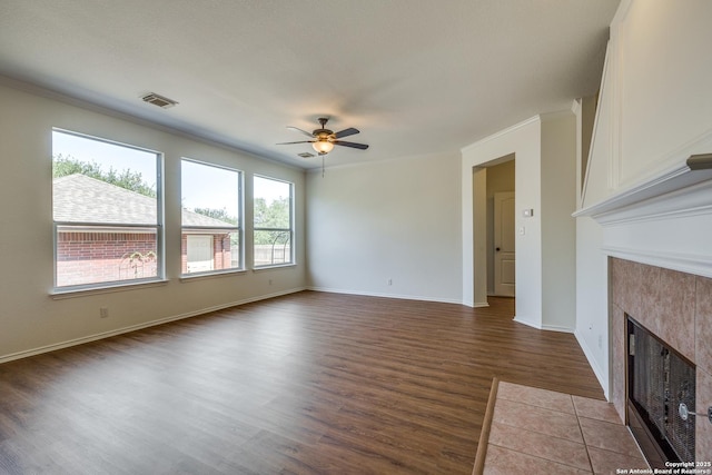 unfurnished living room with a ceiling fan, a tiled fireplace, wood finished floors, ornamental molding, and baseboards