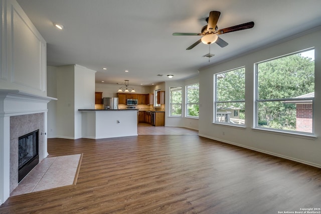 unfurnished living room featuring a chandelier, a tiled fireplace, baseboards, ceiling fan, and wood finished floors