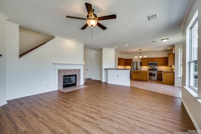 unfurnished living room featuring a ceiling fan, light wood-style flooring, a fireplace with flush hearth, recessed lighting, and a chandelier