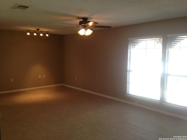 empty room featuring a ceiling fan, baseboards, a textured ceiling, rail lighting, and tile patterned floors