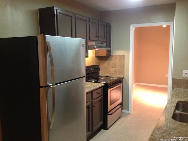 kitchen featuring freestanding refrigerator, electric range, under cabinet range hood, tasteful backsplash, and light stone countertops