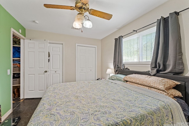 bedroom featuring two closets, finished concrete flooring, and a ceiling fan