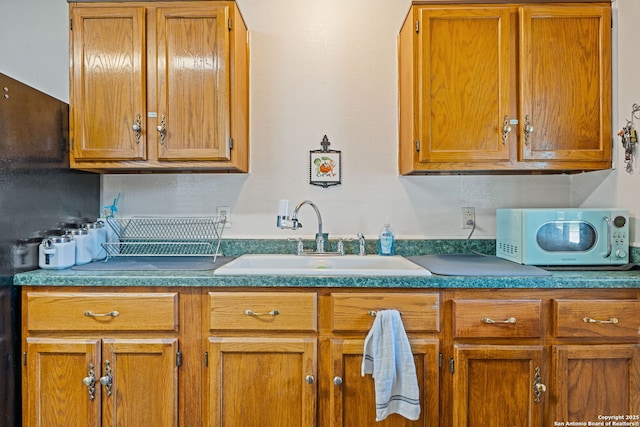 kitchen featuring white microwave, a sink, brown cabinetry, and dark countertops