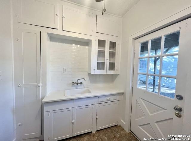 kitchen with a sink, glass insert cabinets, decorative backsplash, and light countertops