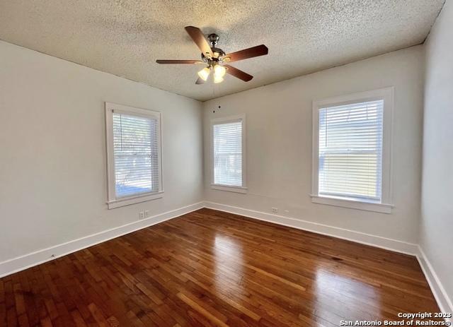 empty room with a textured ceiling, wood finished floors, baseboards, and a ceiling fan