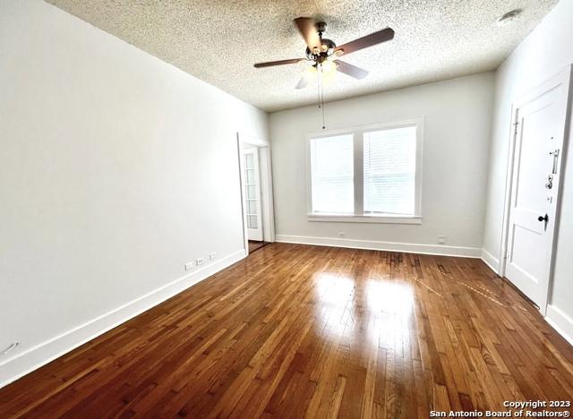 empty room featuring a textured ceiling, a ceiling fan, wood-type flooring, and baseboards