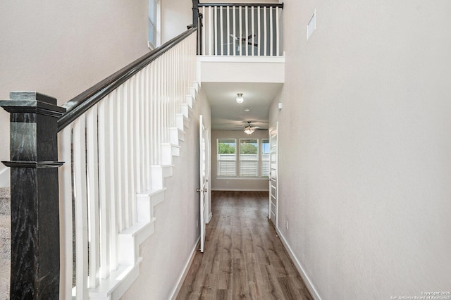 hallway with wood finished floors, baseboards, stairs, and a high ceiling
