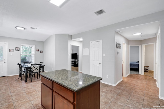 kitchen featuring a kitchen island, light tile patterned floors, baseboards, and dark stone countertops