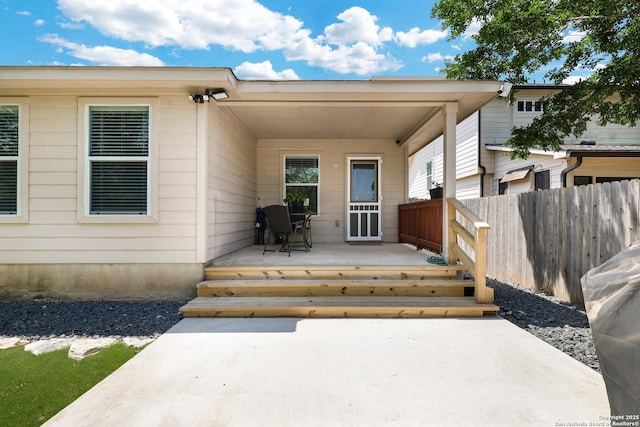 view of exterior entry featuring fence, a patio, and a deck