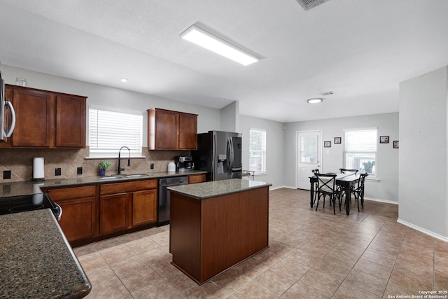 kitchen featuring black appliances, a sink, decorative backsplash, a kitchen island, and plenty of natural light