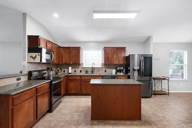 kitchen featuring appliances with stainless steel finishes, a sink, tasteful backsplash, a kitchen island, and baseboards