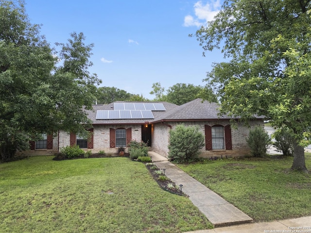 ranch-style home with brick siding, a front yard, and roof mounted solar panels