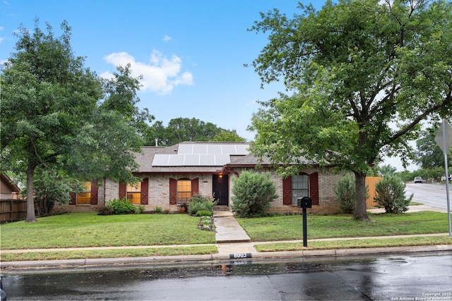 view of front of home featuring solar panels, brick siding, and roof with shingles