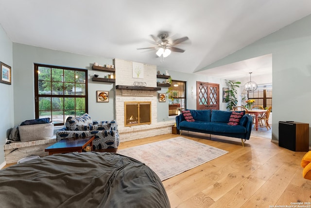 living room with wood-type flooring, ceiling fan, a chandelier, a brick fireplace, and vaulted ceiling