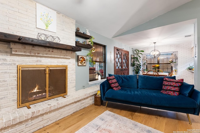 living room featuring wood finished floors, lofted ceiling, a brick fireplace, and a chandelier