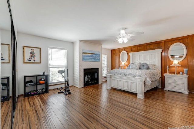 28426 Quadrille Ln, Boerne, TX 78015 - bedroom featuring a glass covered fireplace, wood finished floors, wooden walls, and a ceiling fan