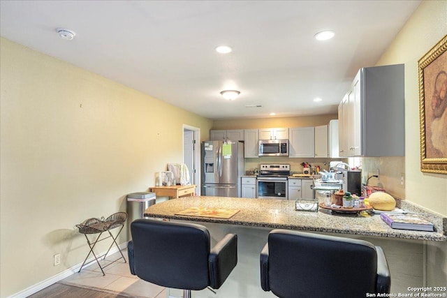 205 Montrose, Liberty Hill, TX 78642 - kitchen with stainless steel appliances, a peninsula, light stone counters, baseboards, and a breakfast bar